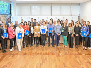 Un grupo de 34 personas posan de pie para la foto, la mayoría de ellos sostiene un folder de color azul en las manos