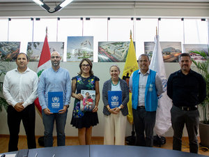 Un grupo de personas posa para la foto en pose institucional, detrás de ellas, unas banderas y unos cuadros.