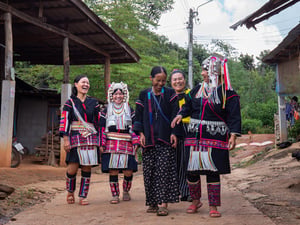 Cinco mujeres en Tailandia que llevan puesta indumentaria típica ríen mientras caminan una a lado de la otra