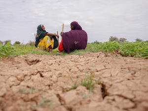 Dos mujeres con la cabeza cubierta platican mientras están sentadas en la tierra