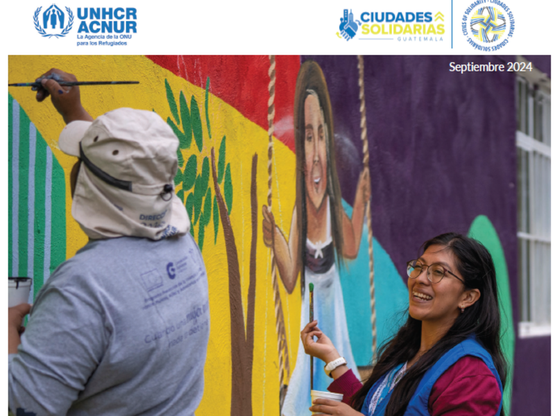 Portada del informe: un hombre que lleva puesto un sombrero y le da la espalda a la cámara pinta un mural; una mujer, que lleva puesto un chaleco de ACNUR y usa anteojos, sonríe mientras observa el trabajo del hombre