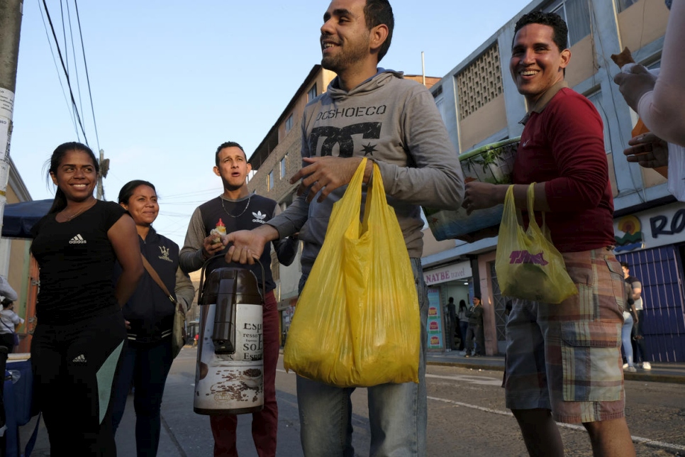 Luis Antonio Pérez (centro), de 24 años, de Barquisimeto, Venezuela, vende chocolate caliente y pan dulce fuera de la sede de Migraciones en Lima, Perú, acompañado por otros vendedores ambulantes de Venezuela. 