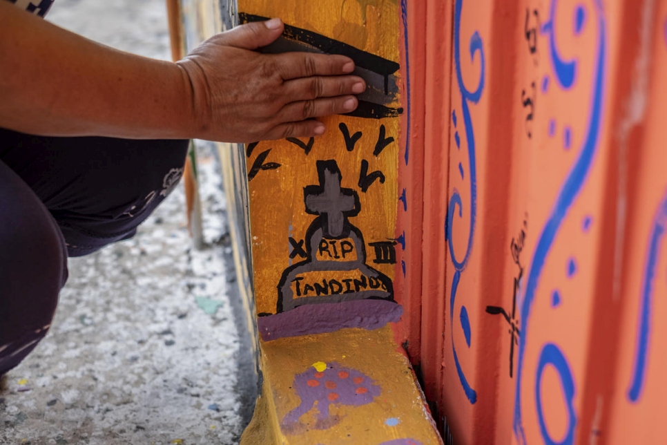 Janeth muestra la tumba que pintó en el mural para expresar su dolor. Su hijo de 17 años fue asesinado por una pandilla criminal en El Salvador en 2017 porque se negó a unirse. 