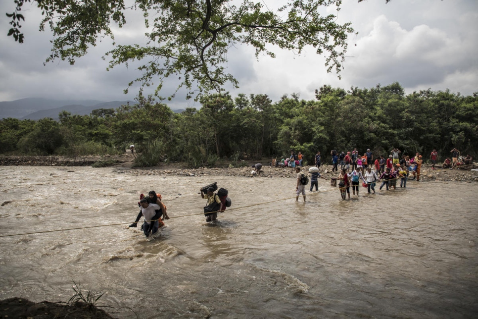 Los refugiados y migrantes venezolanos usan una cuerda para guiarse a través del río Táchira, inundado por la lluvia, para llegar a Cúcuta, Colombia. 