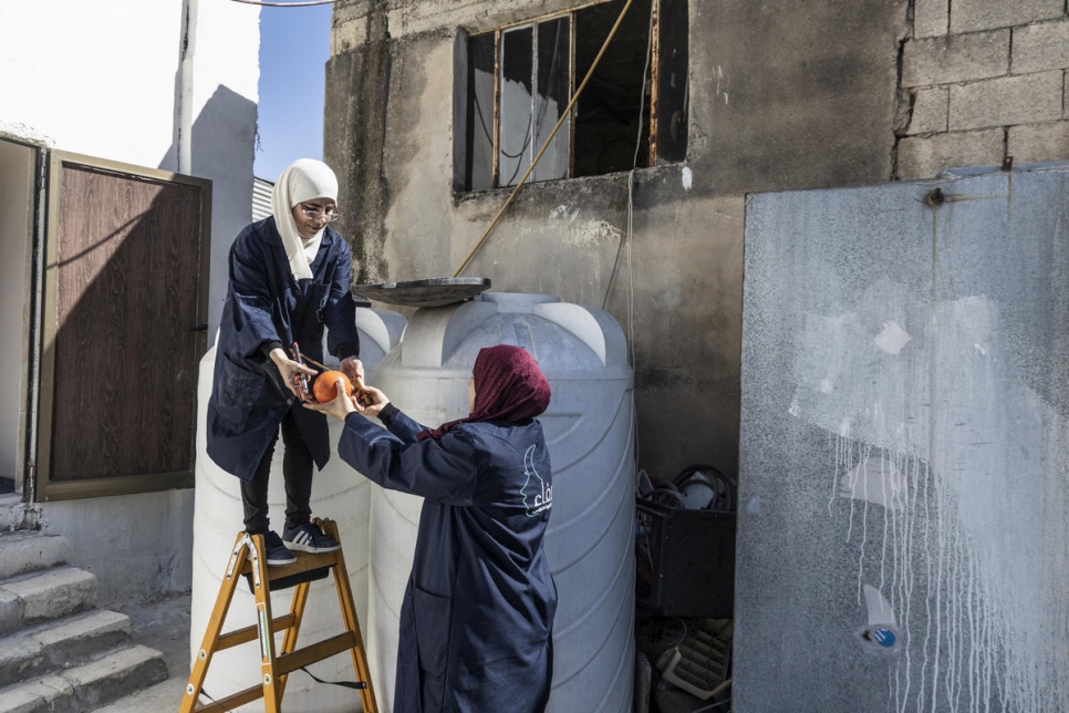 La refugiada siria Buthayna ayuda a Safaa a instalar un tanque de agua en Irbid, Jordania.