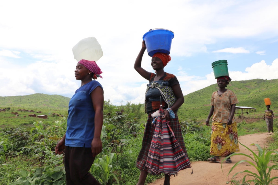 Aisha (delante) vuelve a casa tras ir con otras mujeres a buscar agua a un pozo perforado en el asentamiento de Mulongwe (República Democrática del Congo). 