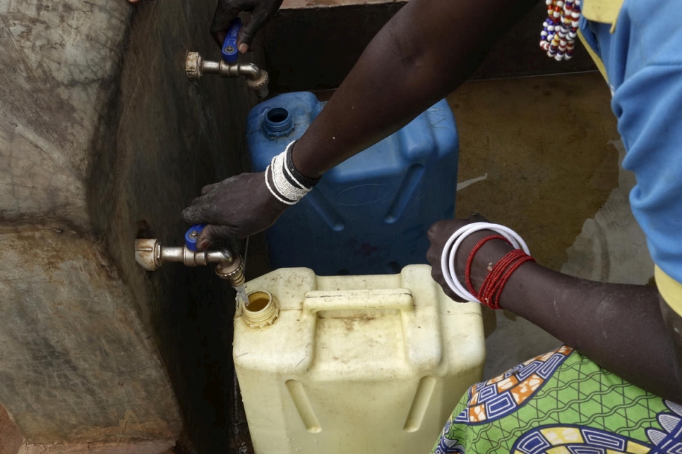 Mujeres de la comunidad local ugandesa rellenan bidones en el punto de distribución de agua establecido para dar servicio tanto a las personas refugiadas como a las comunidades locales en torno al campamento de refugiados de Bidibidi. 