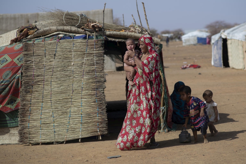Fatima carga a su bebé en el campamento de refugiados de Goudoubo, en Burkina Faso, mientras esperan su turno para la distribución de kits de dignidad.
