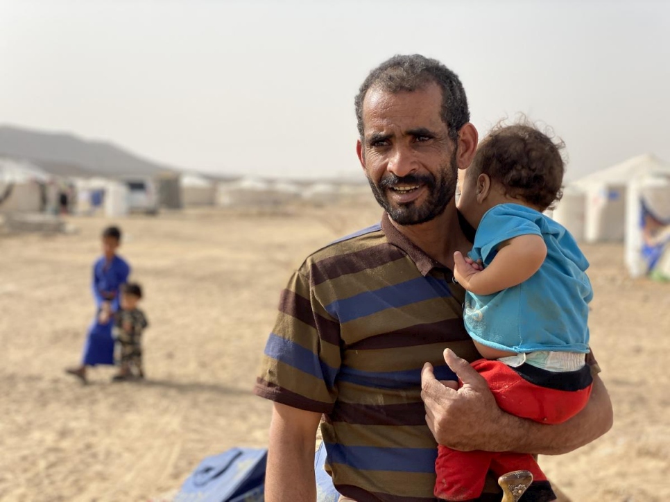 Taher, un yemení de 40 años desplazado por el conflicto, sostiene en brazos a su hijo menor Mustafa, de 2 años, delante de su refugio en el espacio de acogida para desplazados internos en el campamento de Marib.