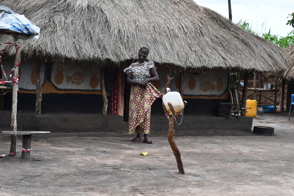 Ferida, una refugiada de Sudán del Sur, se encuentra frente a su casa en el asentamiento de Bele, República Democrática del Congo, con su estación de lavado de manos en primer plano. 