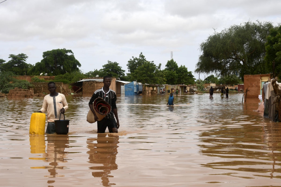 Dos personas llevan sus efectos personales por una calle inundada por el río Níger en el barrio de Kirkissoye, en Niamey, Níger, el 27 de agosto de 2020. 