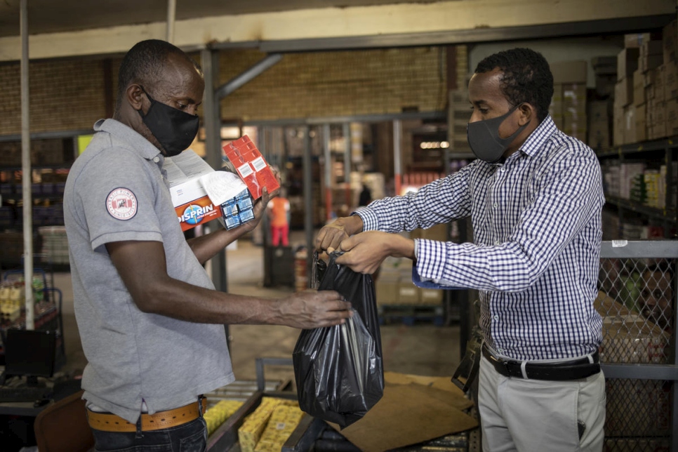 Amin Sheikh (derecha) entrega una bolsa de artículos a un sudafricano vulnerable durante una distribución de alimentos en Pretoria, Sudáfrica. 