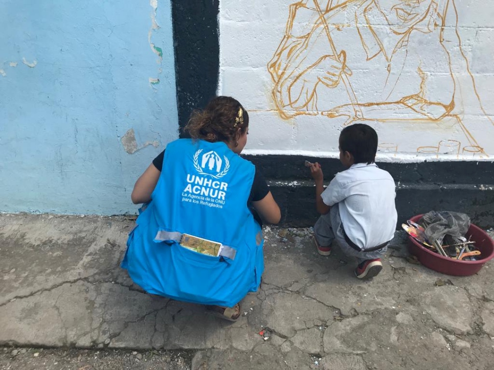 Trabajadora de ACNUR ayuda a un niño a pintar un mural.