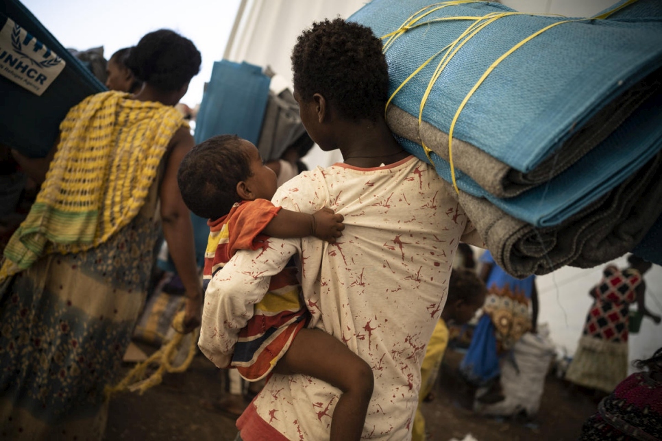 Una refugiada etíope con su bebé recibe esteras y cobijas en un centro de tránsito en Hamdayet, Sudán.