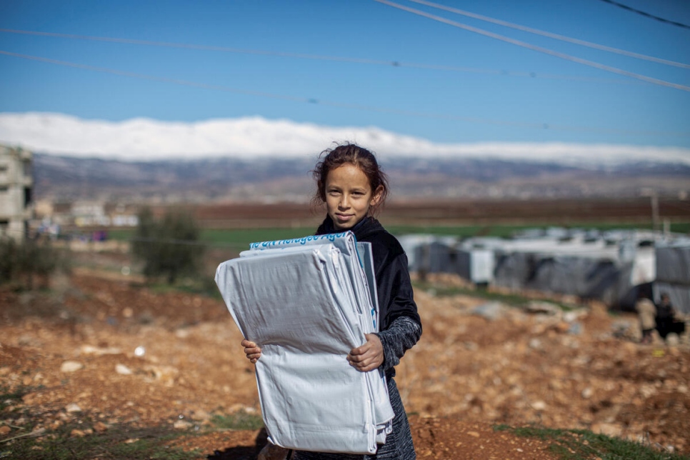 Una joven refugiada siria carga lonas de plástico.
