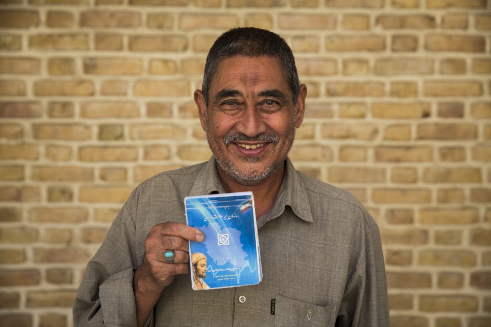 Abdulrahim Rostami, refugiado afgano de 66 años, sostiene el folleto informativo de su seguro de salud en Tehrán, Irán.
