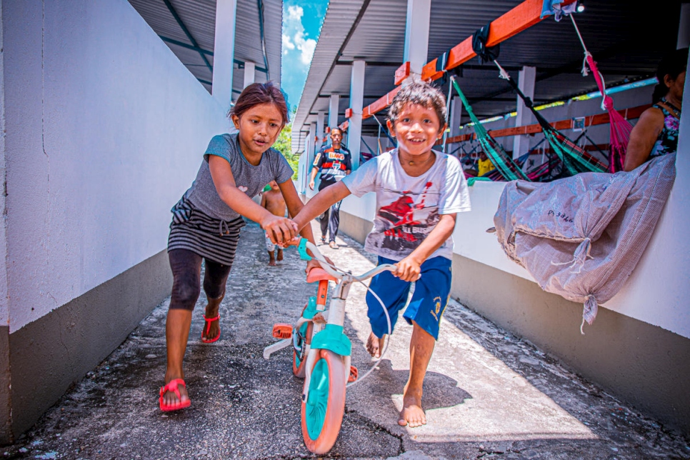 Una niña y un niño venezolanos juegan con una bicicleta en un albergue para personas refugiadas en Manaus, Brasil.
