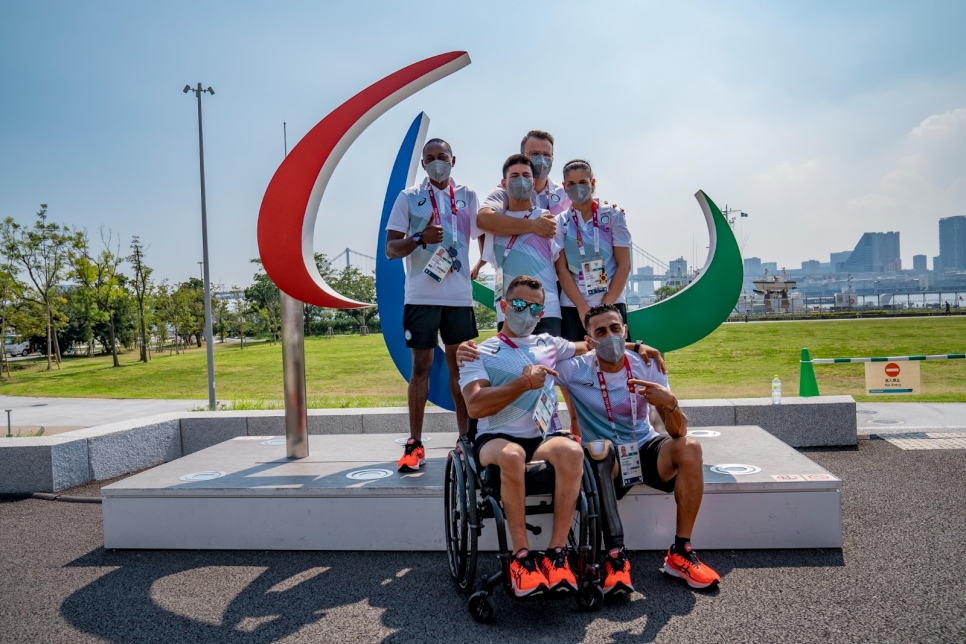 Los seis miembros del Equipo Paralímpico de Atletas Refugiados del CPI se reúnen frente al símbolo de Agitos en Tokio, Japón.