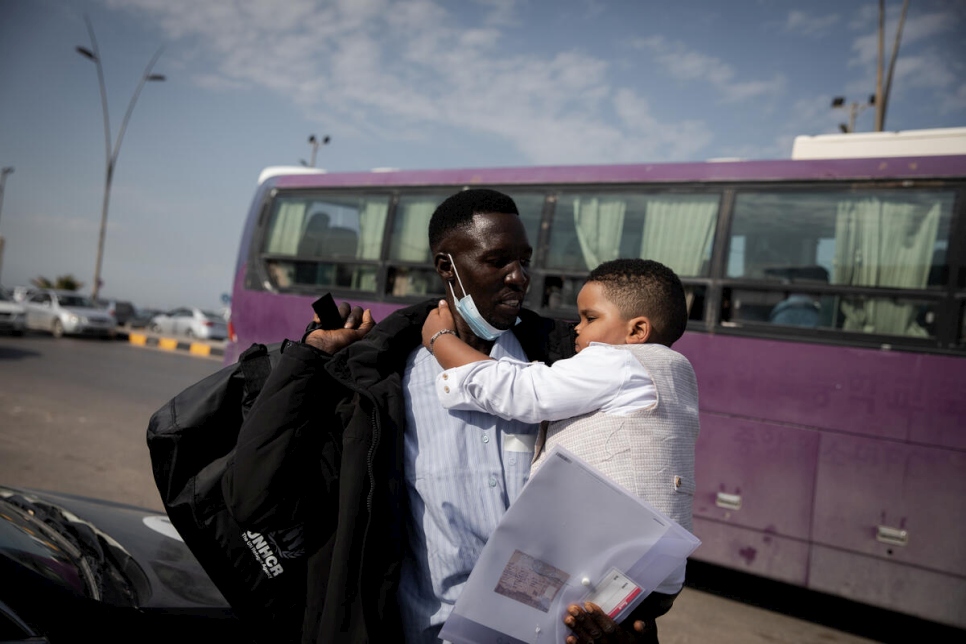 El refugiado sudanés, Osman, ayuda a cargar al hijo pequeño de su compañero de evacuación, Hayat, mientras llegan al aeropuerto de Trípoli para tomar un vuelo contratado por ACNUR con destino a Roma.
