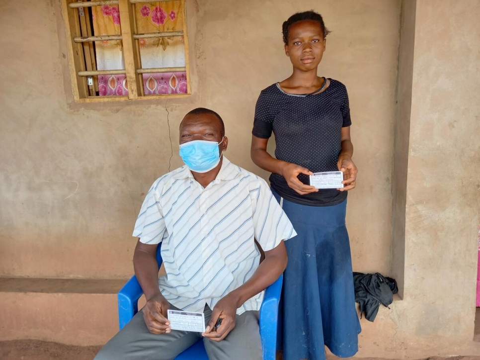 Muanza, de 53 años, sentado junto a su hija, Hélène, quien muestra su certificado de vacunación contra la COVID-19 en el asentamiento de Lóvua, Angola.