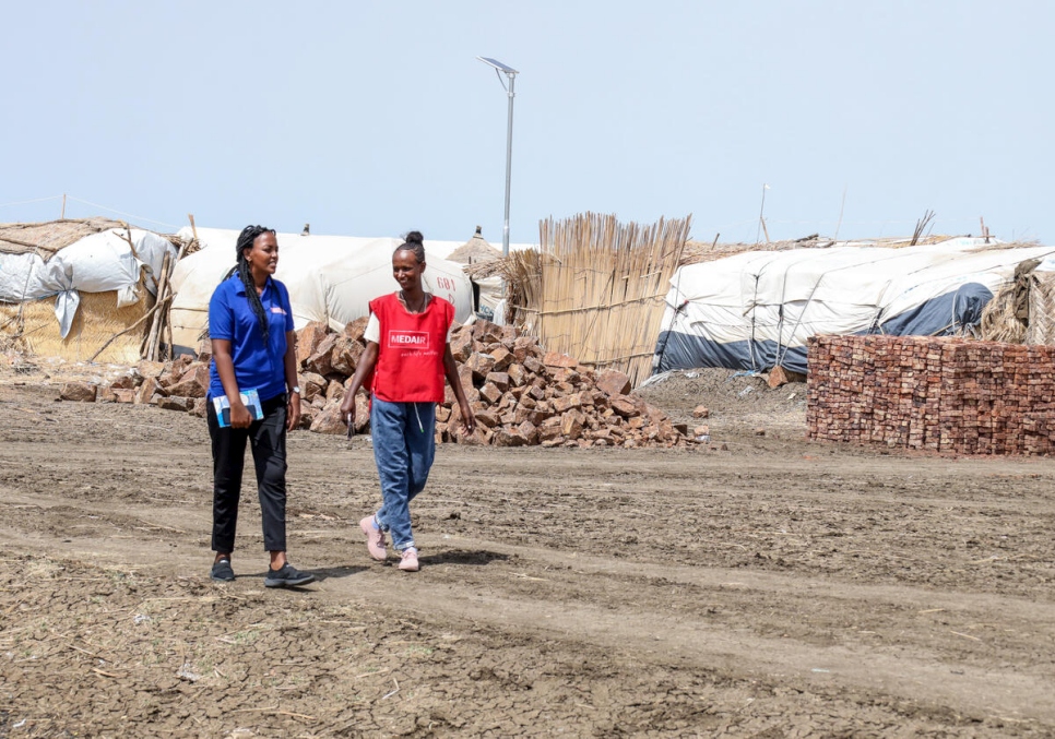 Azmera (izquierda) y Medhn caminan por el campamento de refugiados de Tunaydbah, donde trabajan juntas para construir alojamientos duraderos para otras personas refugiadas.