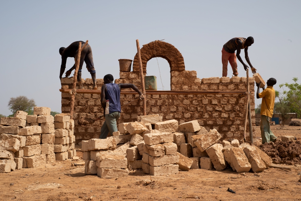Personas desplazadas internas de Burkina Faso reciben capacitación por parte de albañiles locales para construir casas respetuosas con el clima utilizando materiales locales en Kaya, Burkina Faso.