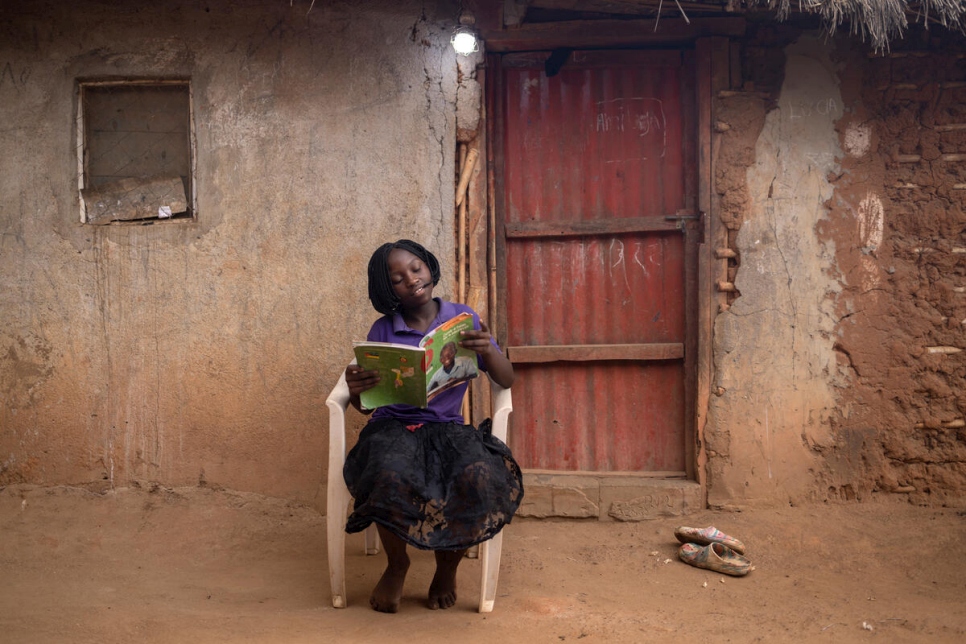 Lucie Songa, de 11 años, lee un libro de texto con luz eléctrica al final del día frente a la casa de su familia en el asentamiento de refugiados de Marratane.