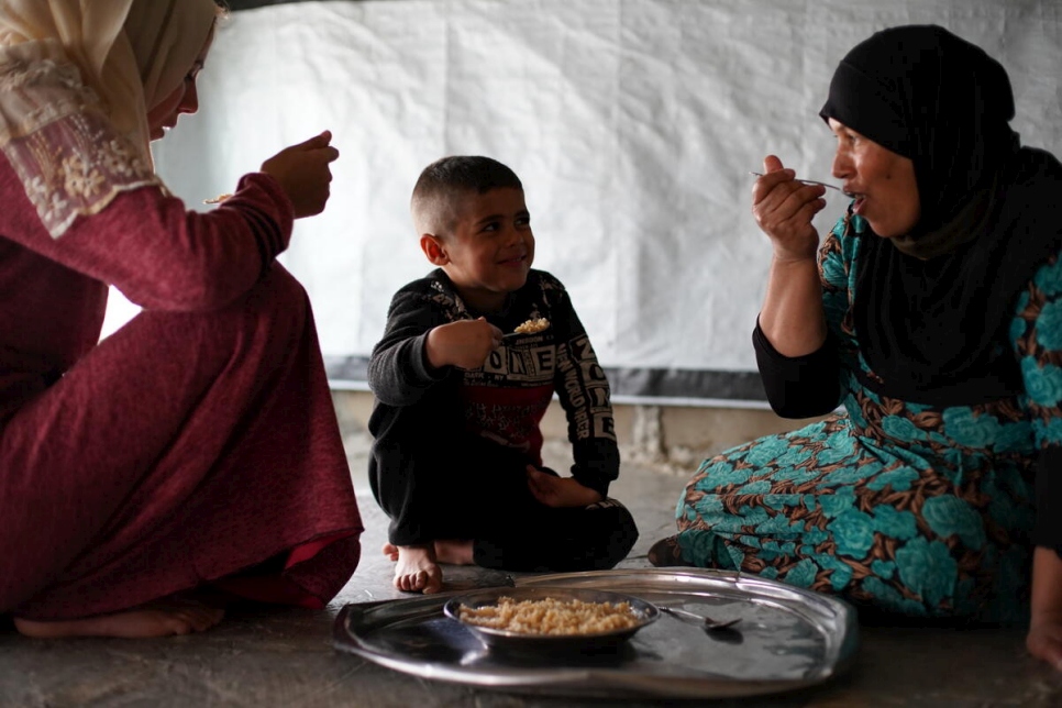 Khadra comparte la comida con su nuera y su sobrino dentro de la tienda de campaña de una sola habitación que la cobija a ella y a otros nueve miembros de su familia.