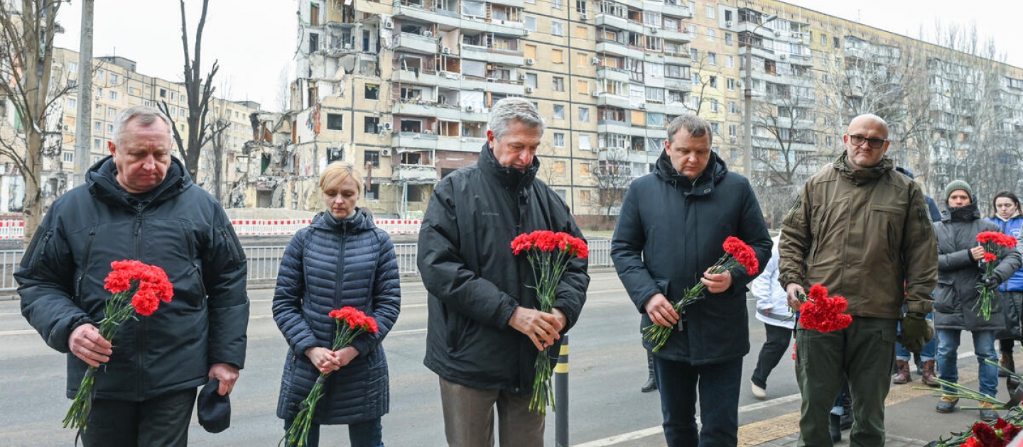 El Alto Comisionado Filippo Grandi (al centro), junto a representantes de las autoridades locales, coloca flores en un edificio residencial destruido durante un ataque con misiles el 14 de enero de 2023, en la ciudad de Dnipro, Ucrania.