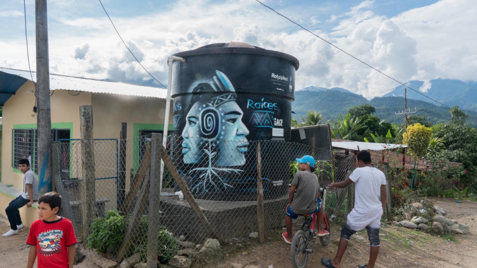 Los niños se paran al lado de un tanque de agua a la entrada de Nueva Esperanza. El tanque, que proporciona agua limpia a la comunidad, se instaló con la ayuda del ACNUR en 2016.