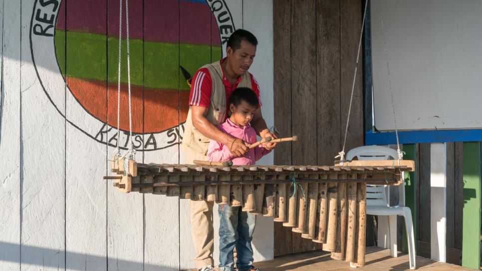 Armando Causaluzan Pai, 38 años, le enseña a su nieto a tocar marimba, un instrumento de percusión de madera, que hace parte del patrimonio cultural awá.