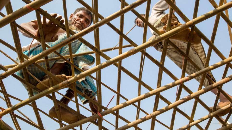 El refugiado Mohammad Ishaq (izq.) refuerza el techo de su albergue con bambú provisto por el ACNUR a los residentes del asentamiento de refugiados de Kutupalong, Bangladesh, antes del monzón.