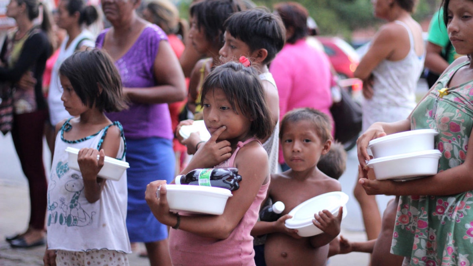 Venezolanos que viven a la intemperie en la plaza Simón Bolívar de Boa Vista haciendo fila en una distribución de comida organizada por miembros de la comunidad local.