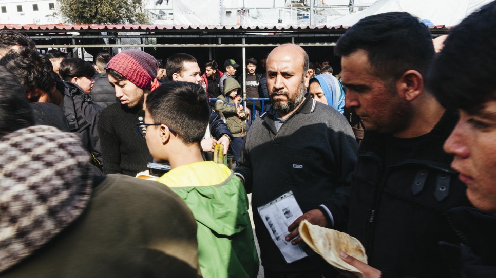 Solicitantes de asilo y migrantes esperan su turno en un punto de distribución de comida en el hacinado centro de recepción e identificación de Moira, en la isla griega de Lesbos.
