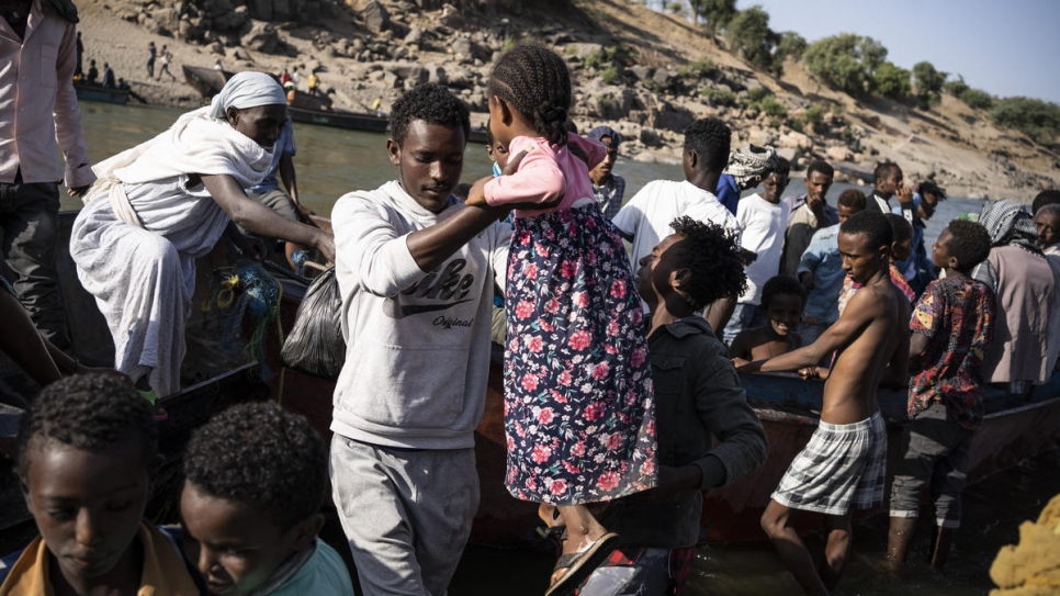 Una niña es sacada en volandas de un barco que traslada personas refugiadas etíopes a través del río Serit, en el paso fronterizo de Hamdayet (Sudán).
