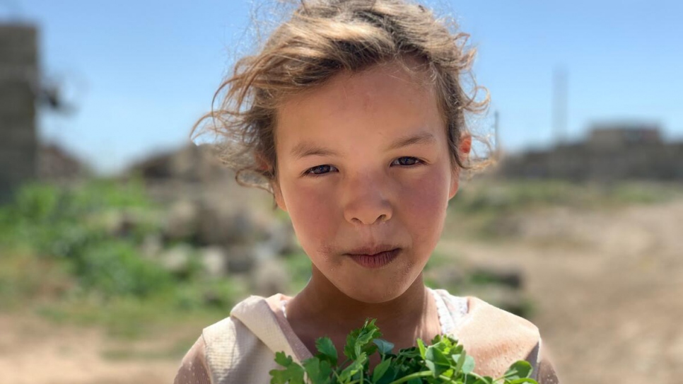 Una niña con un manojo de cilantro frente a su casa dañada en un pueblo cerca de Mosul.