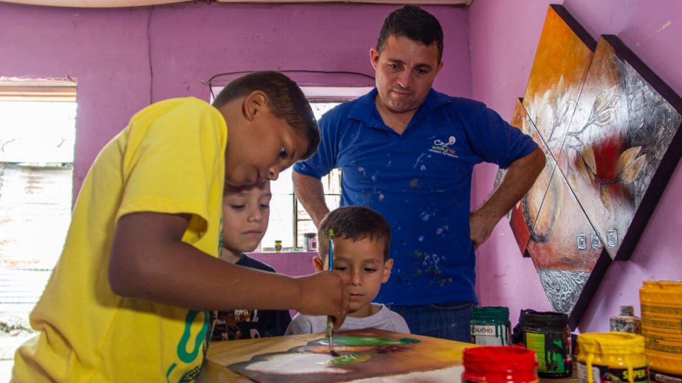 José Soto supervisa a su hijo mayor, quien pinta uno de los lienzos que vende la familia para ganar dinero.