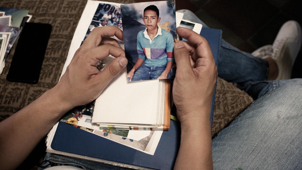 Santiago mira las fotos de su hermano menor que, a los 16 años, fue asesinado por miembros de una pandilla. La tragedia forzó al resto de la familia a huir de su casa.
