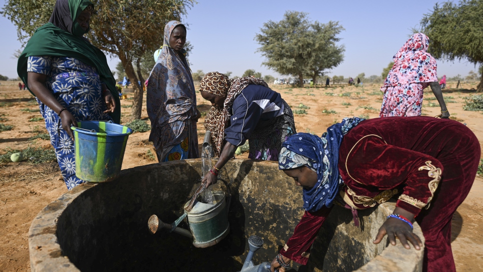 Las mujeres extraen agua de un pozo antes de regar sus plantas.