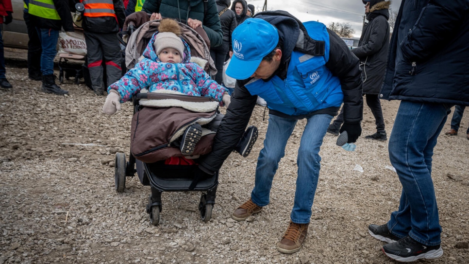 Batyr Sapbyiev, oficial de protección de ACNUR, ayuda a una niña y a su madre en el trayecto a los autobuses en el cruce fronterizo de Palanca, Moldavia.
