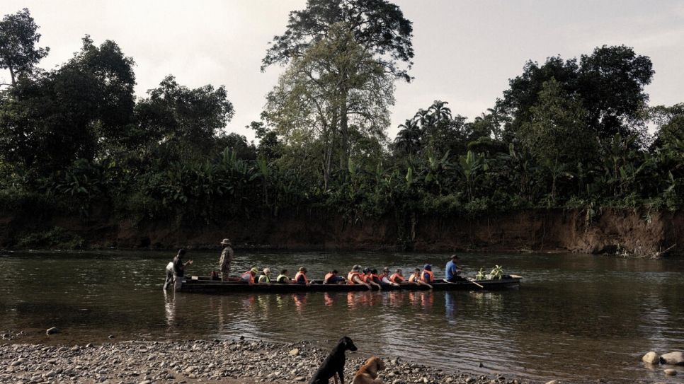 Personas refugiadas y migrantes se suben a una canoa en el río Membrillo, mientras un oficial del Servicio Nacional de Fronteras de Panamá hace su registro.