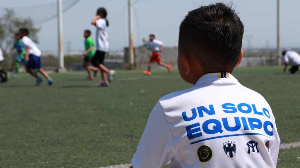 Niño observa el juego de sus compañeros mientras espera su turno para participar en las ligas sociales de fútbol que forman parte de las actividades de coexistencia pacífica de ACNUR en Nuevo León.