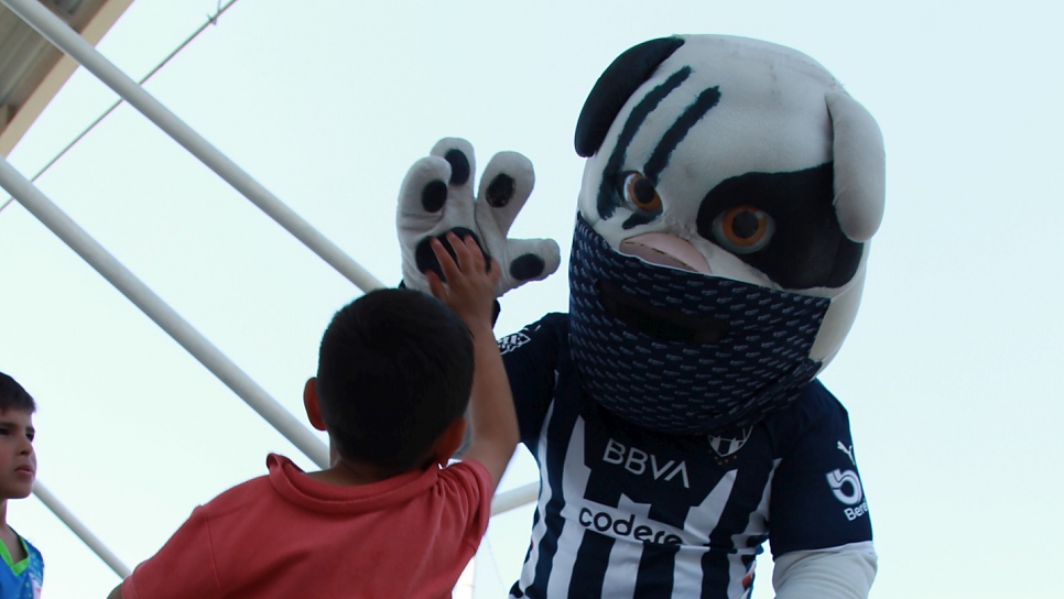 Monty, la mascota del club de fútbol Monterrey saluda a niño durante las ligas sociales.