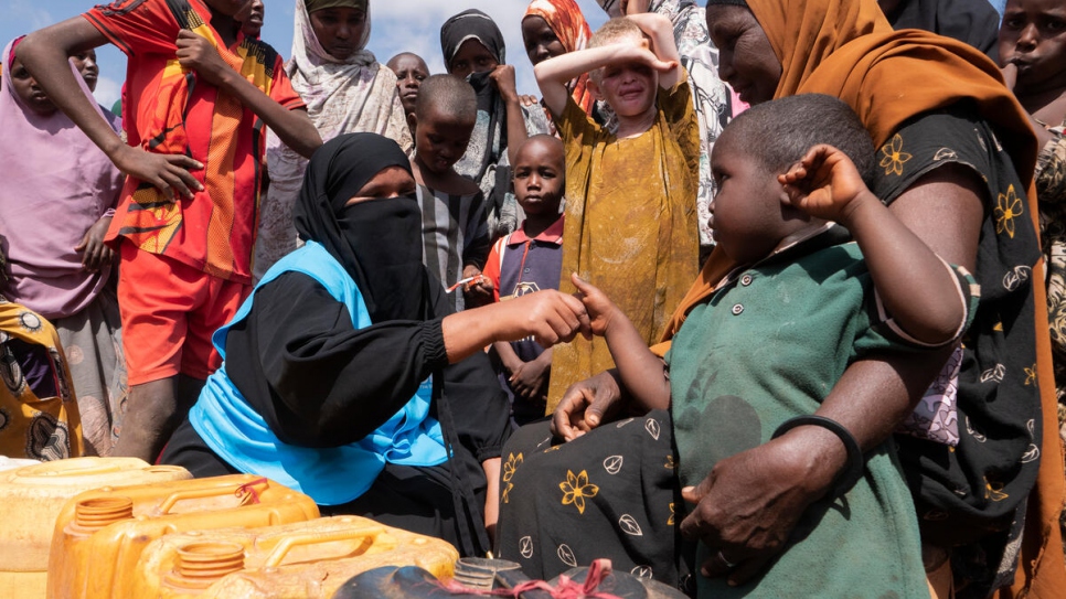 Mujeres, niñas y niños llenan bidones con agua en un asentamiento de desplazados internos en Dolow.