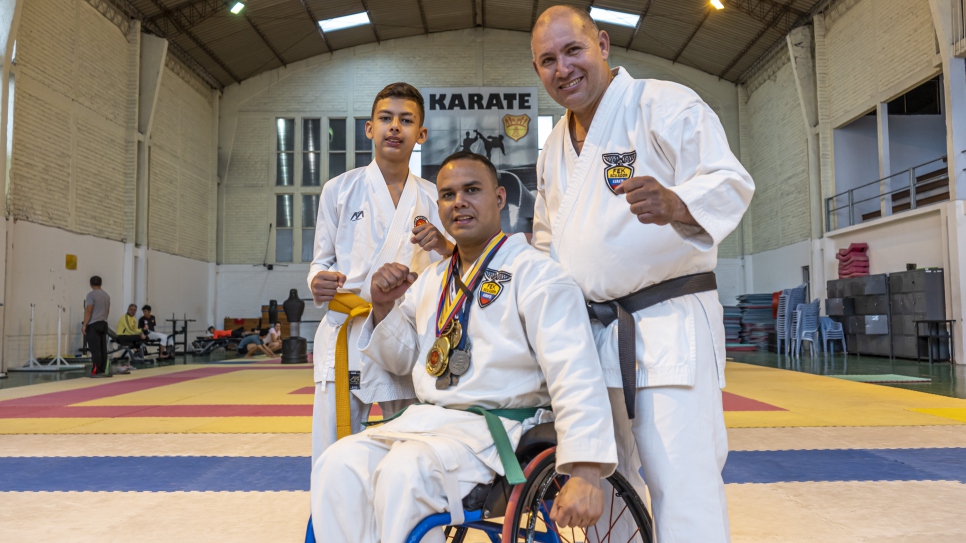 Carlos Acosta, su hijo Carlos Raúl, refugiados venezolanos, y Rainy Camacho, instructor venezolano de para-karate, sonríen juntos al final del entrenamiento en Quito.