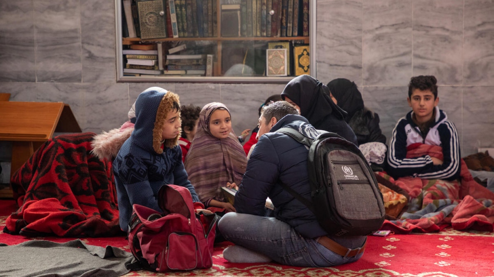 Un trabajador de ACNUR habla con un niño y su familia, albergados en la mezquita del barrio de Suleiman Al-Halabi de Alepo, Siria.