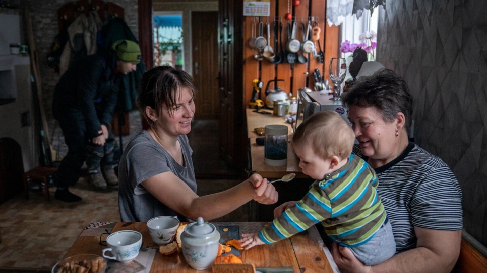 Svitlana, de 29 años, alimenta a su hijo de siete meses, Matvii, que está sentado en brazos de su abuela Olena mientras su padre Mykhailo se prepara para salir de casa.