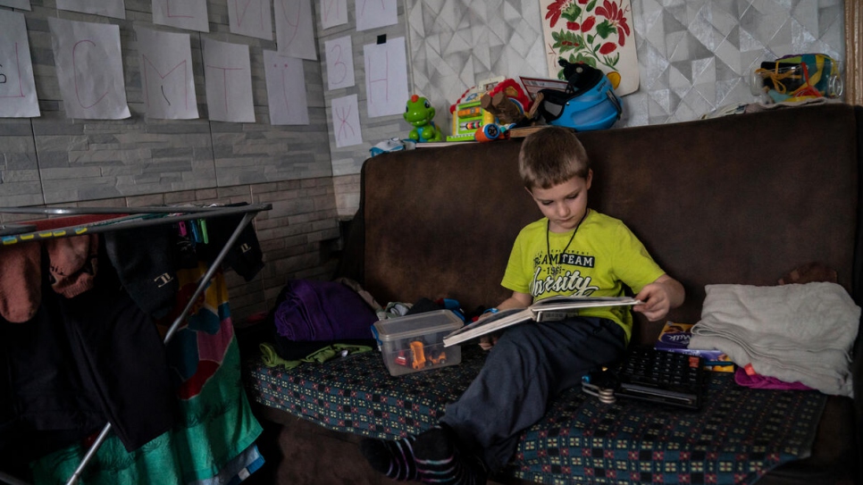 Ivan, de 5 años, hojea un libro en la cocina de sus bisabuelos, donde han pegado el alfabeto ucraniano en las paredes para ayudarle a aprender.