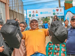 Un grupo de personas posa para la foto en la calle con al centro un hombre que muestra dos maletas sonriendo.