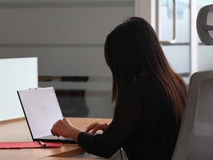 Una mujer de espaldas escribiendo en una computadora.